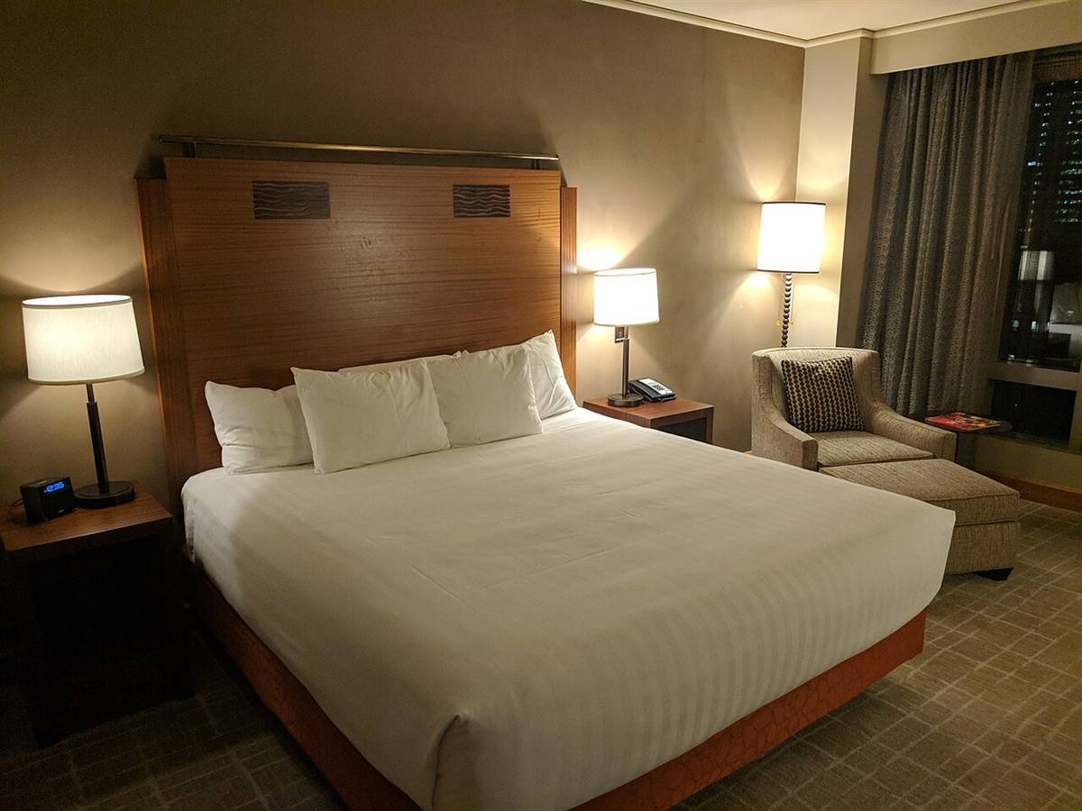 Neatly made bed with white pillows in a softly lit bedroom with bedside lamps in the evening