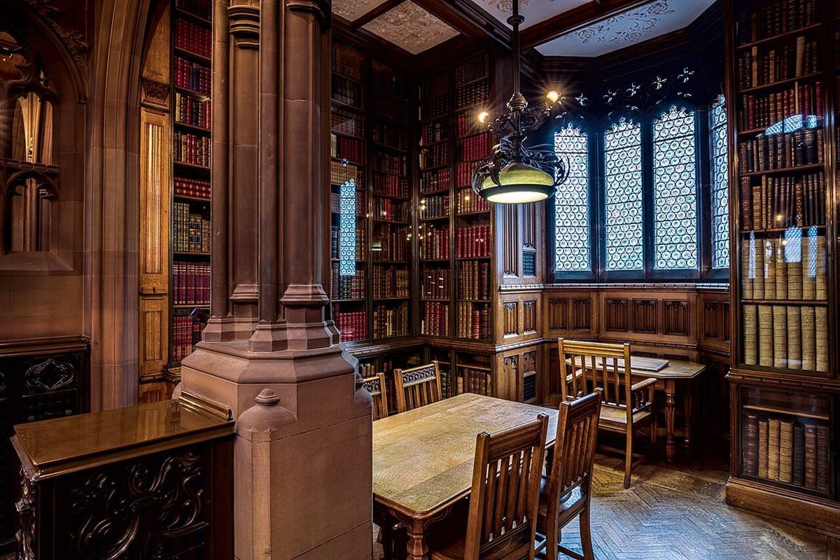 Quiet library study room with wooden tables, chairs and tall shelves of old books